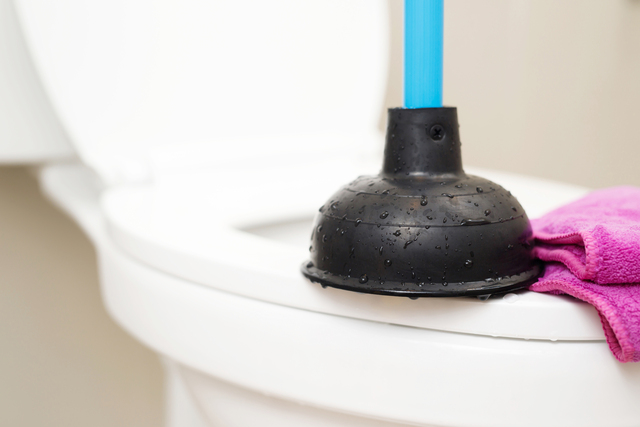 A serviceman is repairing a toilet with a hand plunger caused by a clogged toilet.